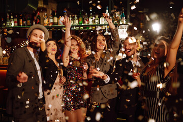 Happy friends throwing confetti and jumping while enjoying party. Group of  young people...