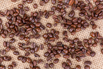 Background scattered roasted brown coffee beans over a burlap textured cloth