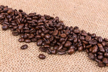 Diagonal line of roasted brown coffee beans over a burlap textured cloth