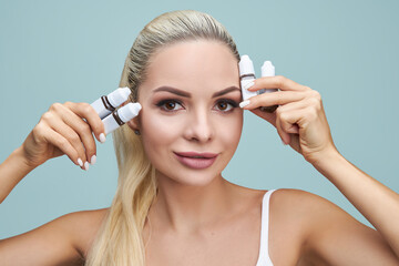 A blonde girl holds pigments near her face for a premature eyebrow makeup. Fashion, beauty, makeup,...