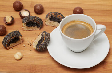 Cookie with poppy seeds on cutting board and white cup of black coffee