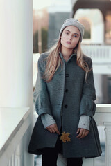 blond girl in knitted hat and coat with maple leaf close up portrait on city architecture background