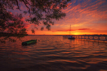 Krajobraz wodny. Czerwony zachód słońca nad jeziorem z żaglówkami