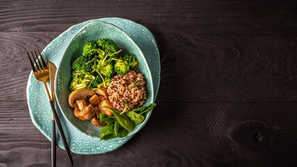 Green vegan salad from vegetables broccoli, mushrooms, spinach and quinoa in a bowl. Delicious breakfast or snack on a dark background, top view