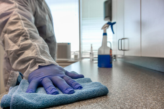 Person with PPE protective suit uses sanitizer wiping and cleaning the surface