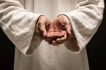 Water for Baptism pouring out of the hands of Jesus Christ during a dark night.