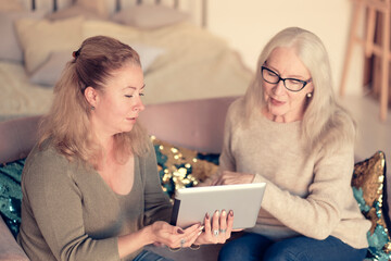 Woman teaching senior mother to use internet at home. Senior woman with her daughter looking at modern gadget indoors. relaxing together, different generations hobby pastime. support for the elderly