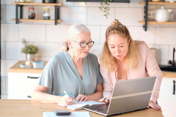Fototapeta na wymiar daughter helps her elderly mother figure it out online with her personal account. Woman teaching senior mother to use internet at home. Senior woman with her daughter looking at modern gadget indoors.