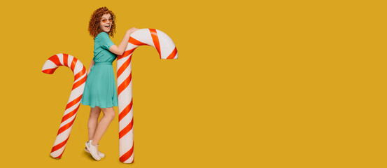 Red-haired curly woman with waw emotions stands near candy canes on fortuna gold background....