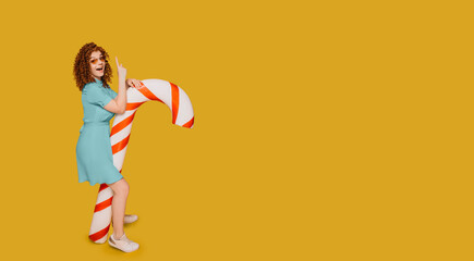 Red-haired curly woman with waw emotions stands near candy cane on fortuna gold background....