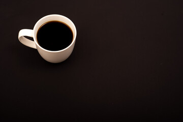 Top view of white ceramic mug with black coffee on black background. Copy space