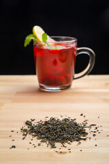 A cup of berry tea with lemon and tea leaves scattered on the table.