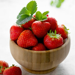 Fresh strawberries in wooden bowl with green leaves.