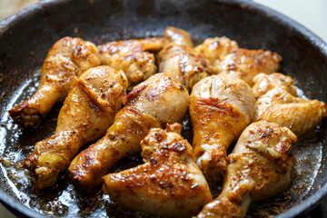 Chicken drumsticks and wings marinated in soy sauce in a pan.