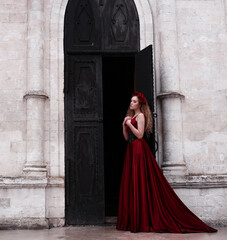 Girl in long red dress standing near church's black door