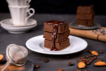 Cocoa brownies pouring with melted dark chocolate on a white plate. Black background