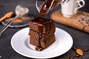 Cocoa brownies pouring with melted dark chocolate on a white plate. Black background