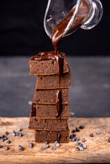 Cocoa brownies pouring with melted dark chocolate on a white plate. Black background