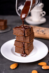 Cocoa brownies pouring with melted dark chocolate on a white plate. Black background