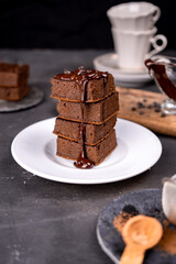 Cocoa brownies pouring with melted dark chocolate on a white plate. Black background