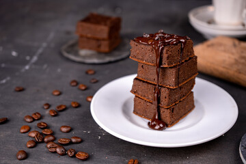 Cocoa brownies pouring with melted dark chocolate on a white plate. Black background