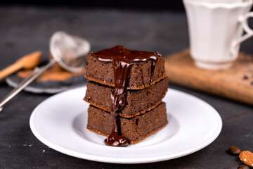 Cocoa brownies pouring with melted dark chocolate on a white plate. Black background