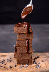 Cocoa brownies pouring with melted dark chocolate on a white plate. Black background