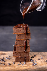 Cocoa brownies pouring with melted dark chocolate on a white plate. Black background