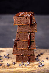 Cocoa brownies pouring with melted dark chocolate on a white plate. Black background
