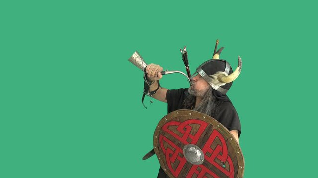 Portrait mature viking in helmet with horns signals the battle. Warrior with shield blows the horn on green background