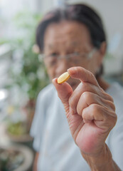 Close up view of aged senior asian female's hand holding a vitamin tablet with fingers.
Healthcare concept with medicines.
Selective Focus.