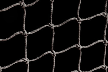 A woven net made of strong brown rope cotton, creating a regular pattern over a black background.
