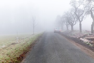 Fototapeta premium Dangerous driving. Slippery road. Driving car on a rainy and foggy day. Autumn road. Car on the road in the fog. Autumn landscape.