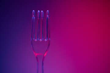 Plastic transparent fork on purple background