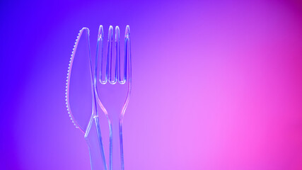 Plastic transparent knife and fork on purple background