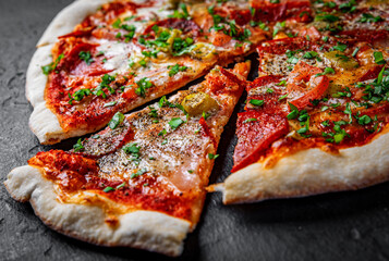 Pizza with Mozzarella cheese, ham, tomato sauce, pepper, salami. Italian pizza on Dark grey black slate background