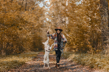 Fototapeta premium Stylish woman training white dog in sunny autumn woods. Cute swiss shepherd puppy learning