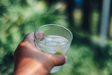 Holding a drink  and ice in the glass against yard green background in summer
