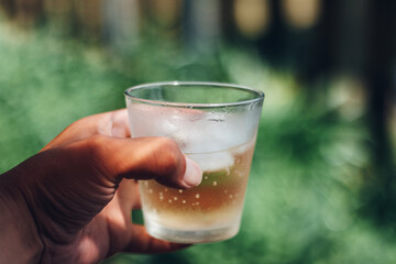 Holding a drink  and ice in the glass against yard green background in summer
