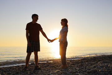 Lovers smile and look at each other in the rays of the setting sun on the seashore. Happy relationship together