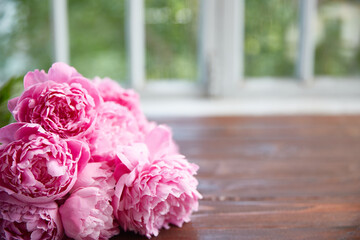 Empty Wooden table background with place for text or present product. Pink peonies on a dark table against the background of a defocus window.