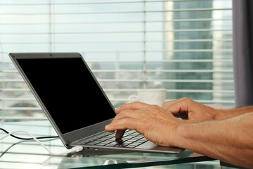 man works behind a laptop with blank screen in an office in front of a window in a modern European city, the concept of business ideas, workplace