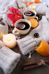 two cups of hot mulled wine with lemon, persimmon and tangerine fruits, candles, box with gift in kraft paper, with red bow lies on table, concept of holiday, congratulations merry christmas, new year