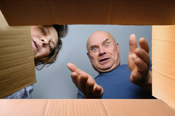 woman and a man opened a cardboard box with an ordered product, look into it, emotionally reacts to...