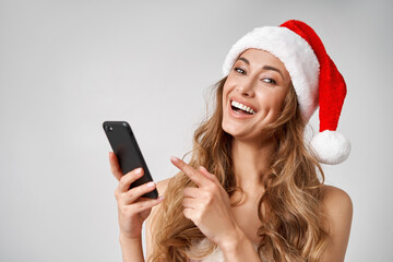 Naklejka premium Woman christmas Santa Hat white studio background with smartphone in hand