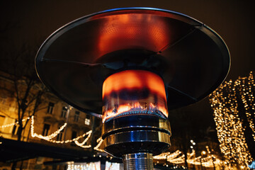 Closeup shot of a gas-burning outdoor patio heater with Christmas lights in the background