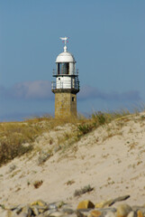 View of a lighthouse behind a sand dune on a sunny day.
