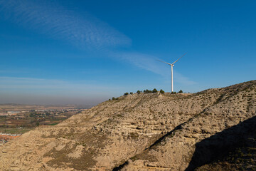 Isolated wind turbine on top of a hill with semi-desert landscape and a valley in the background