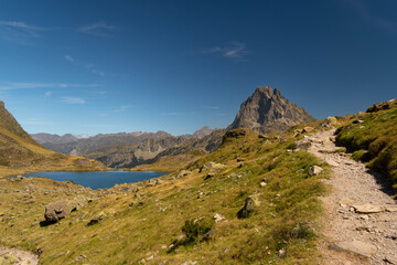 Fototapeta na wymiar Mountain path with a lake and the Midi d'Ossau peak in the background surrounded by mountains and nature