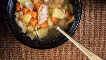 chicken soup with vegetables in a black dish with a spoon